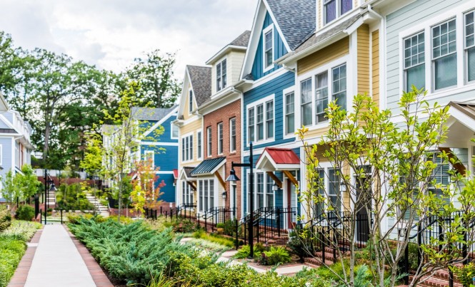 Row of colorful, red, yellow, blue, white, green painted residential townhouses, homes, houses with brick patio gardens in summer